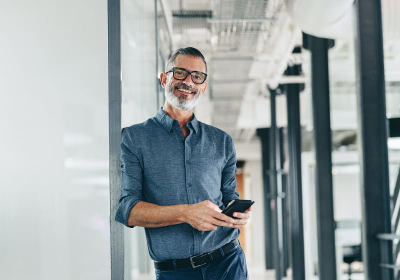 A smiling colleague standing in an open office corridor with a phone in hand