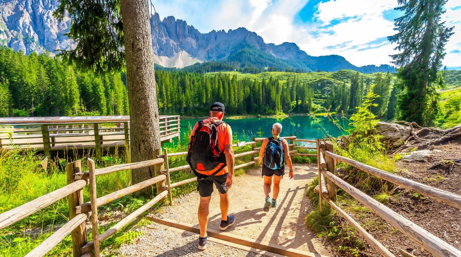 Walkers on mountain path towards a turquoise alpine lake in the Dolomites, Trentino Alto Adige, Italy