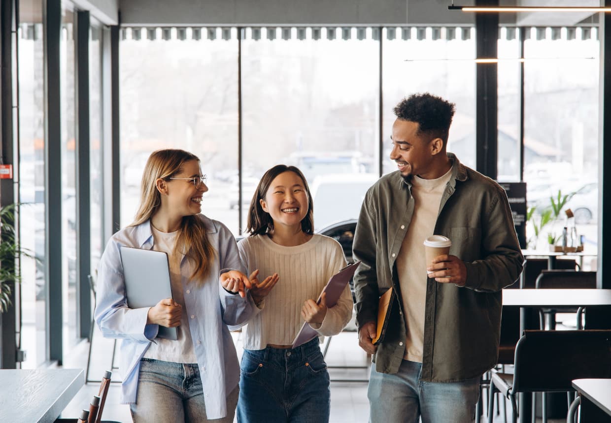 コーヒータイムを楽しみ、談笑しながら、ノートパソコンやノートを手にオフィス内を歩く3人の大学生。