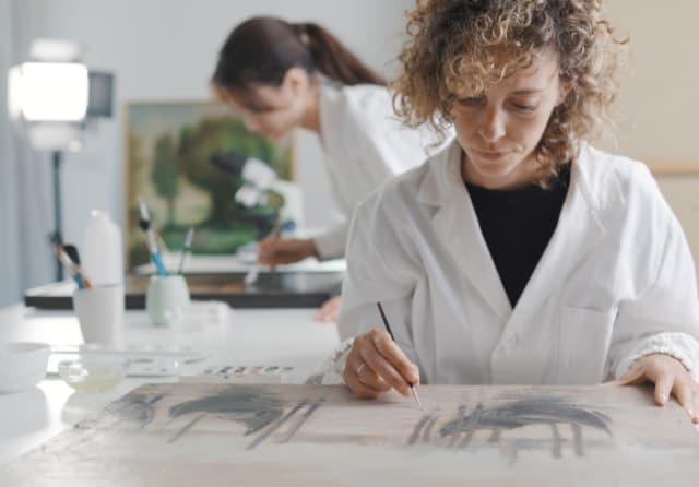 Art conservation student carefully restoring a painting with a fine paintbrush in a museum studio fieldwork placement.