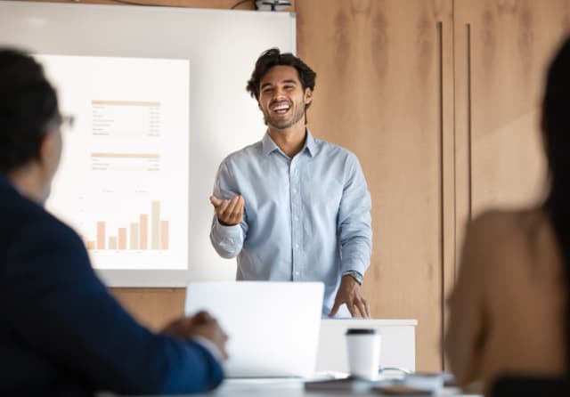 Confident young student presenting findings to peers at a corporate-style meeting, showcasing growing academic confidence.