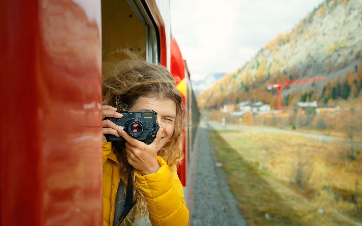 A traveller photographing the autumn mountain landscape from a scenic train.