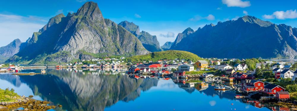 Colorful coastal village reflecting in clear blue water, framed by mountains.