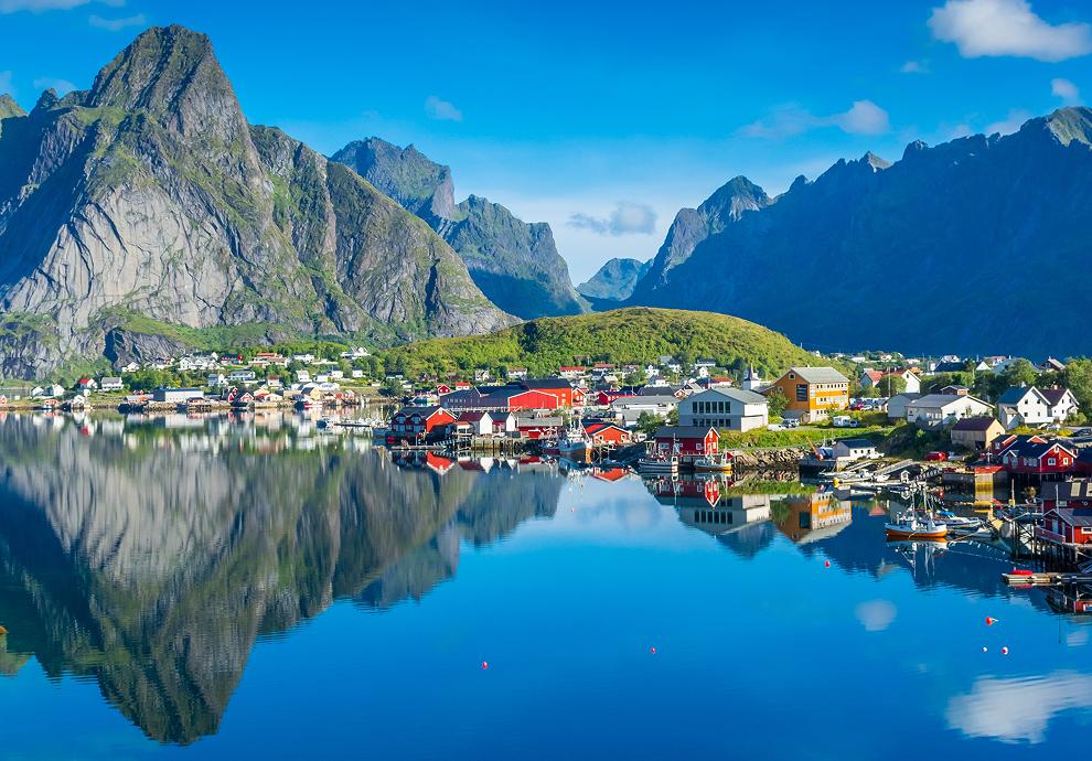Colorful coastal village reflecting in clear blue water, framed by mountains.