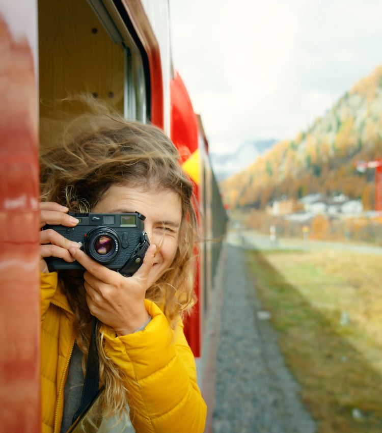 A traveller photographing the autumn mountain landscape from a scenic train.