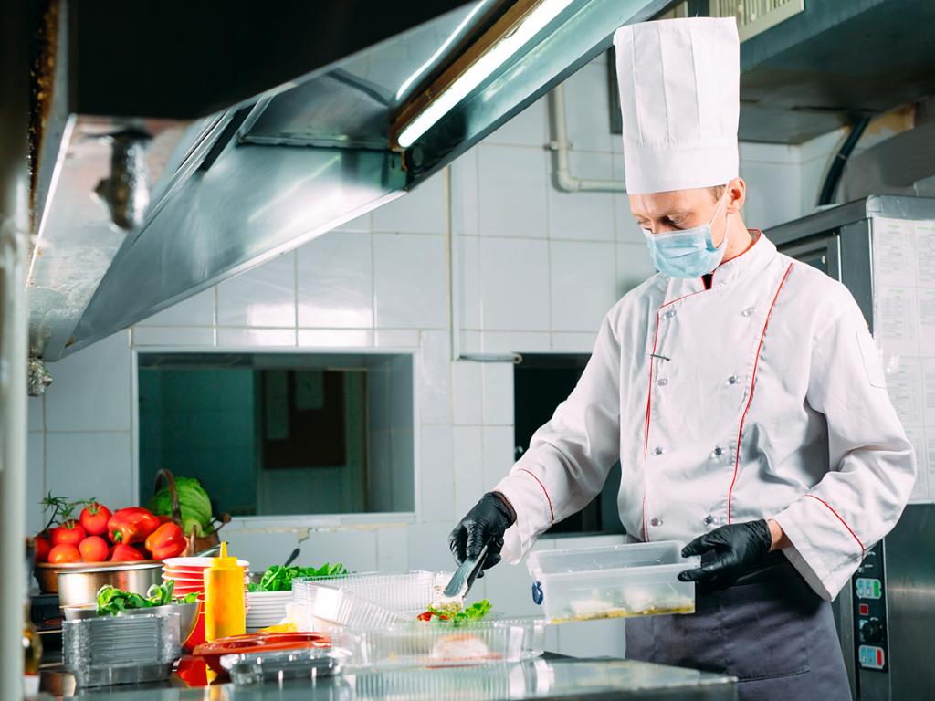 Chef preparing food in kitchen whilst wearing face mask