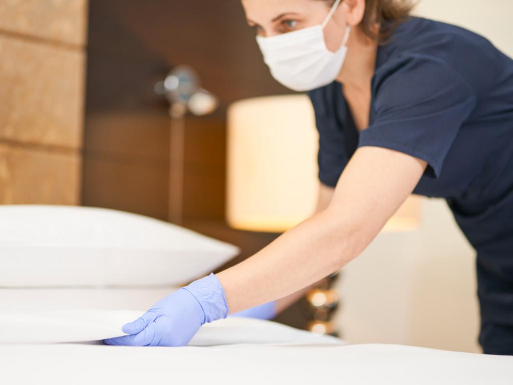 Maid in hotel making a bed wearing gloves and a face mask